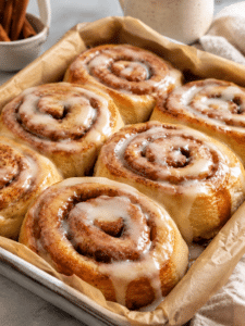 Overhead photo of easy soft and fluffy sourdough discard cinnamon rolls fresh from the oven with cream cheese frosting on a white ceramic dish.